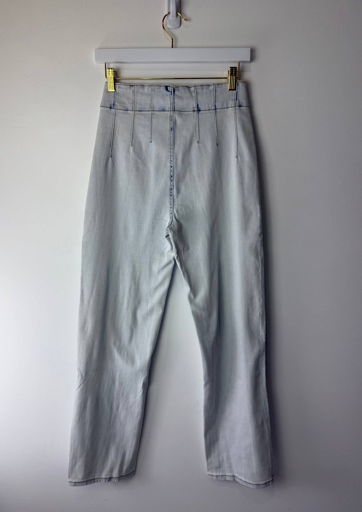 Light blue pants hanging on a white hanger against a plain background
