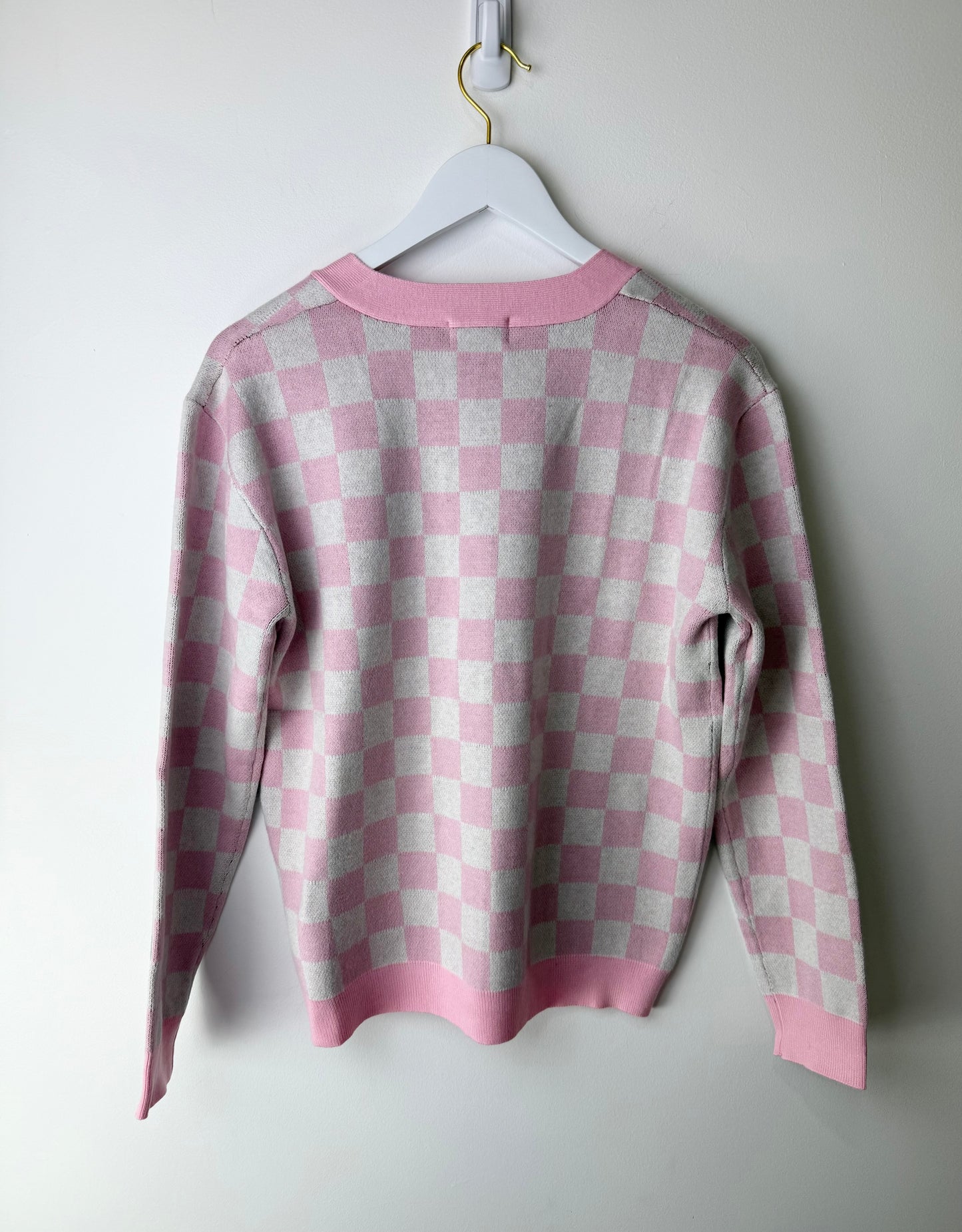 Pink and gray checkered sweater on a white hanger against a light gray background