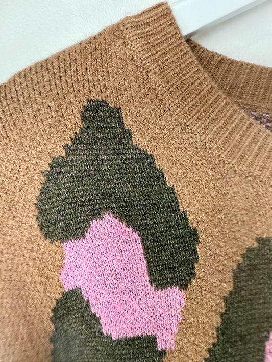Close-up of a brown knitted sweater with green and pink abstract design on a light background