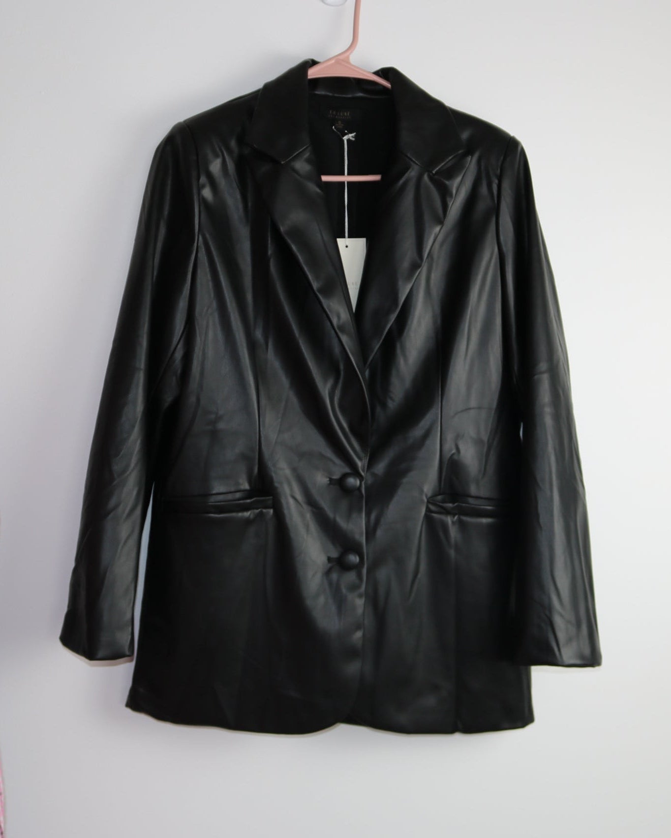 A faux leather blazer hanging on a hanger against a white background.