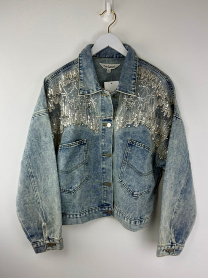 Denim jacket with sequin embellishments on a white hanger against a white background