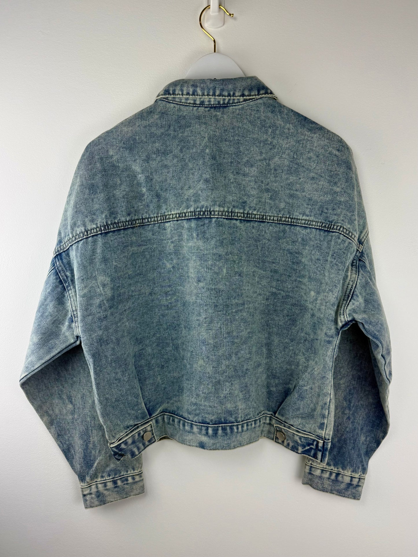 Blue denim jacket on a white hanger against a white background