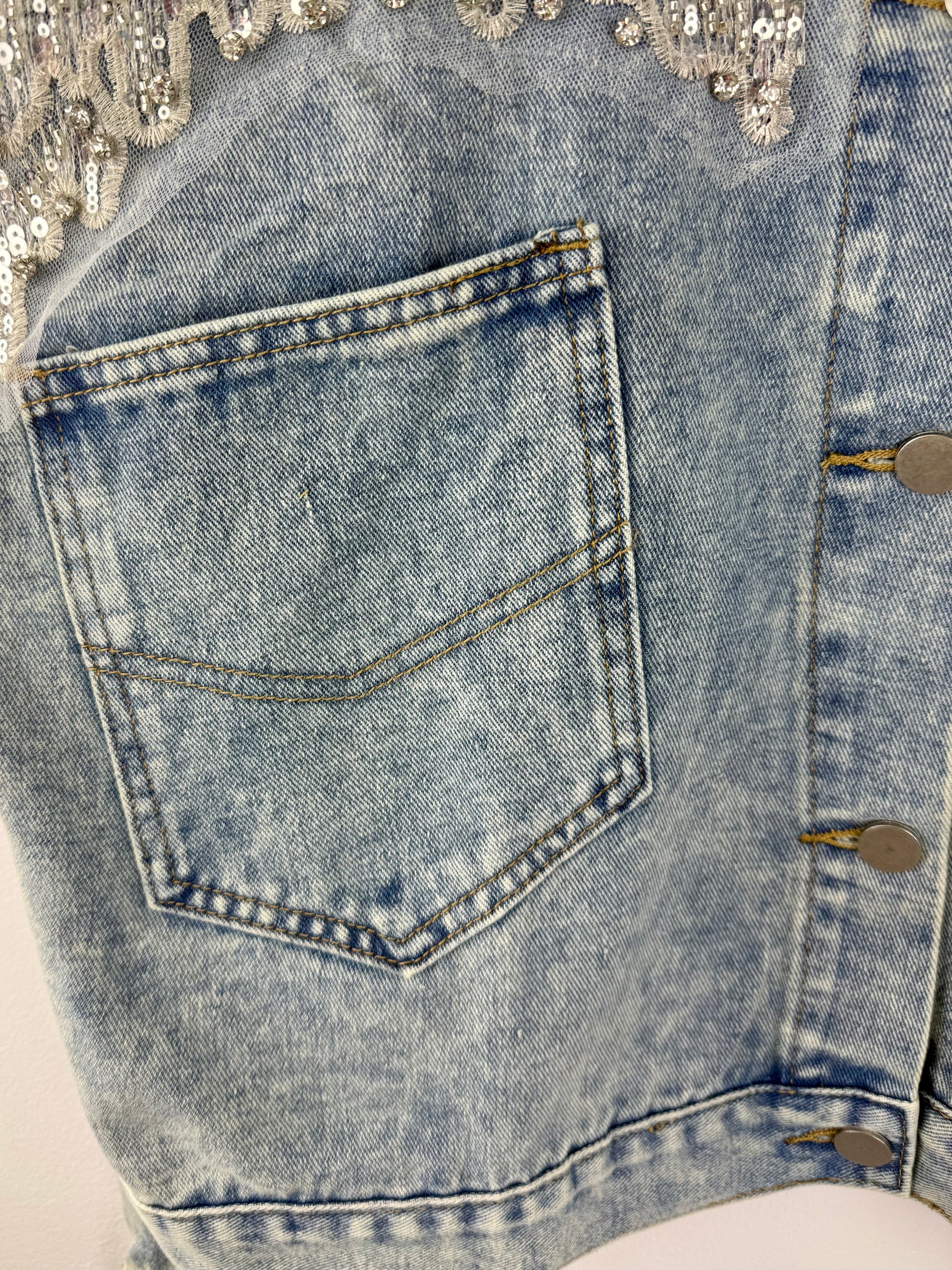Close-up of a blue denim jacket with a pocket and decorative elements.