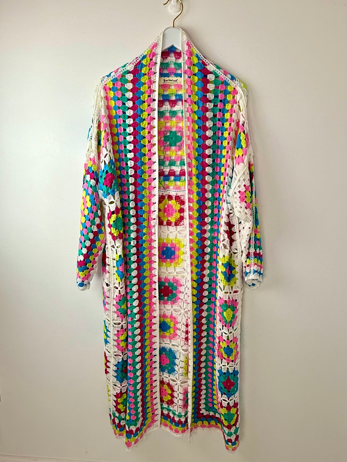Colorful crochet cardigan on a hanger against a white background