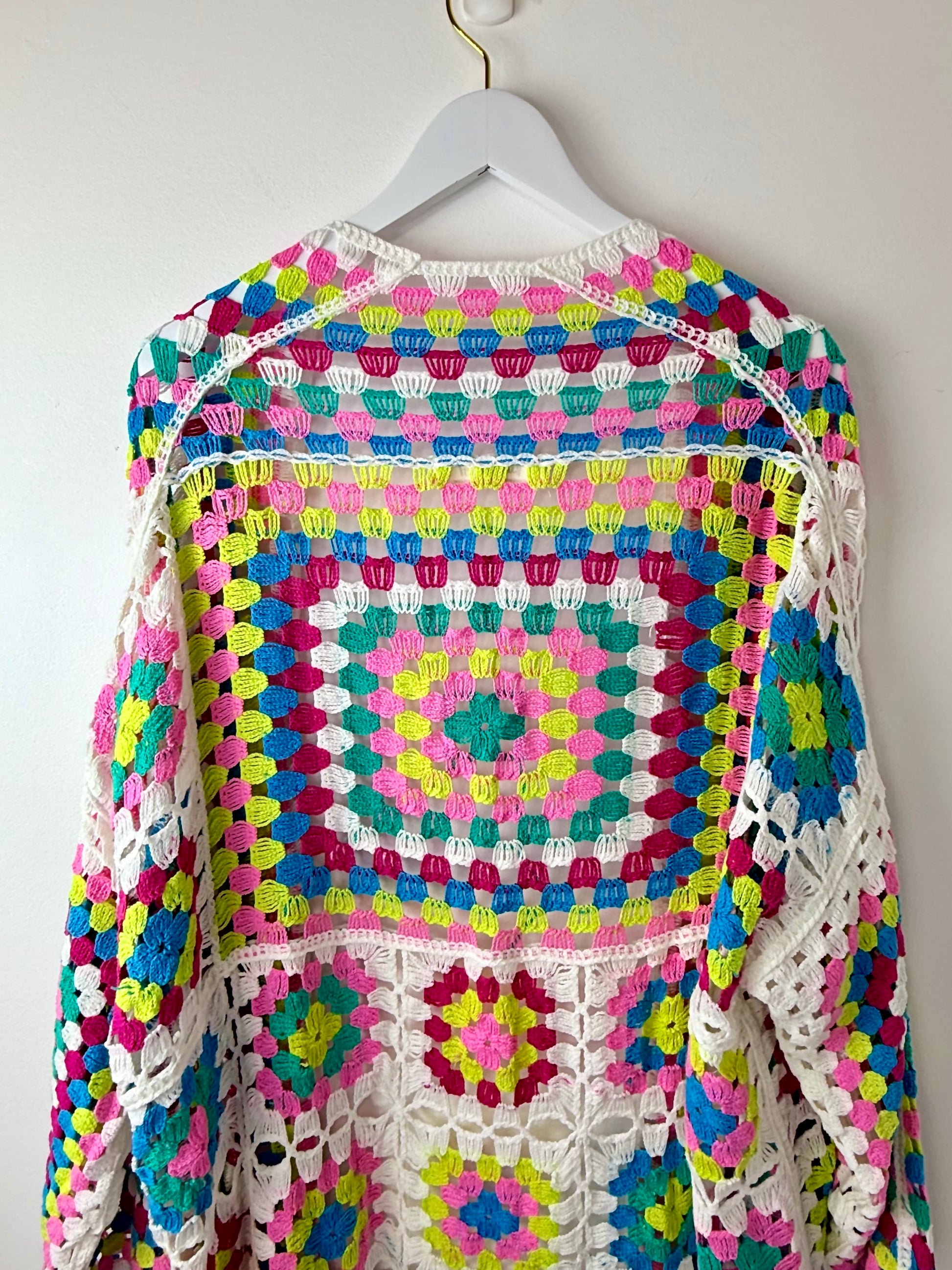 Colorful crocheted sweater on a hanger against a white background
