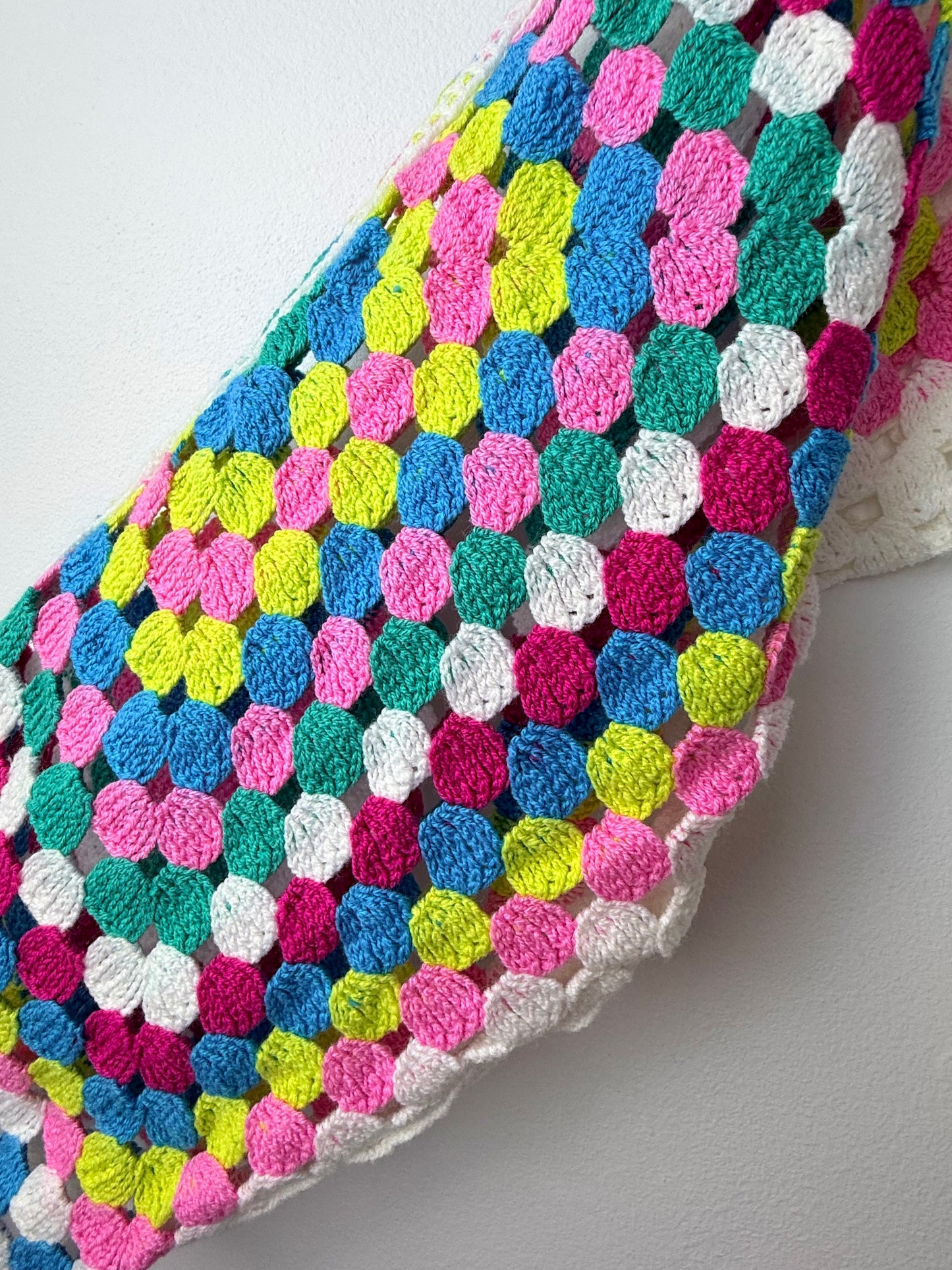 Colorful crocheted blanket with a geometric pattern on a light gray background