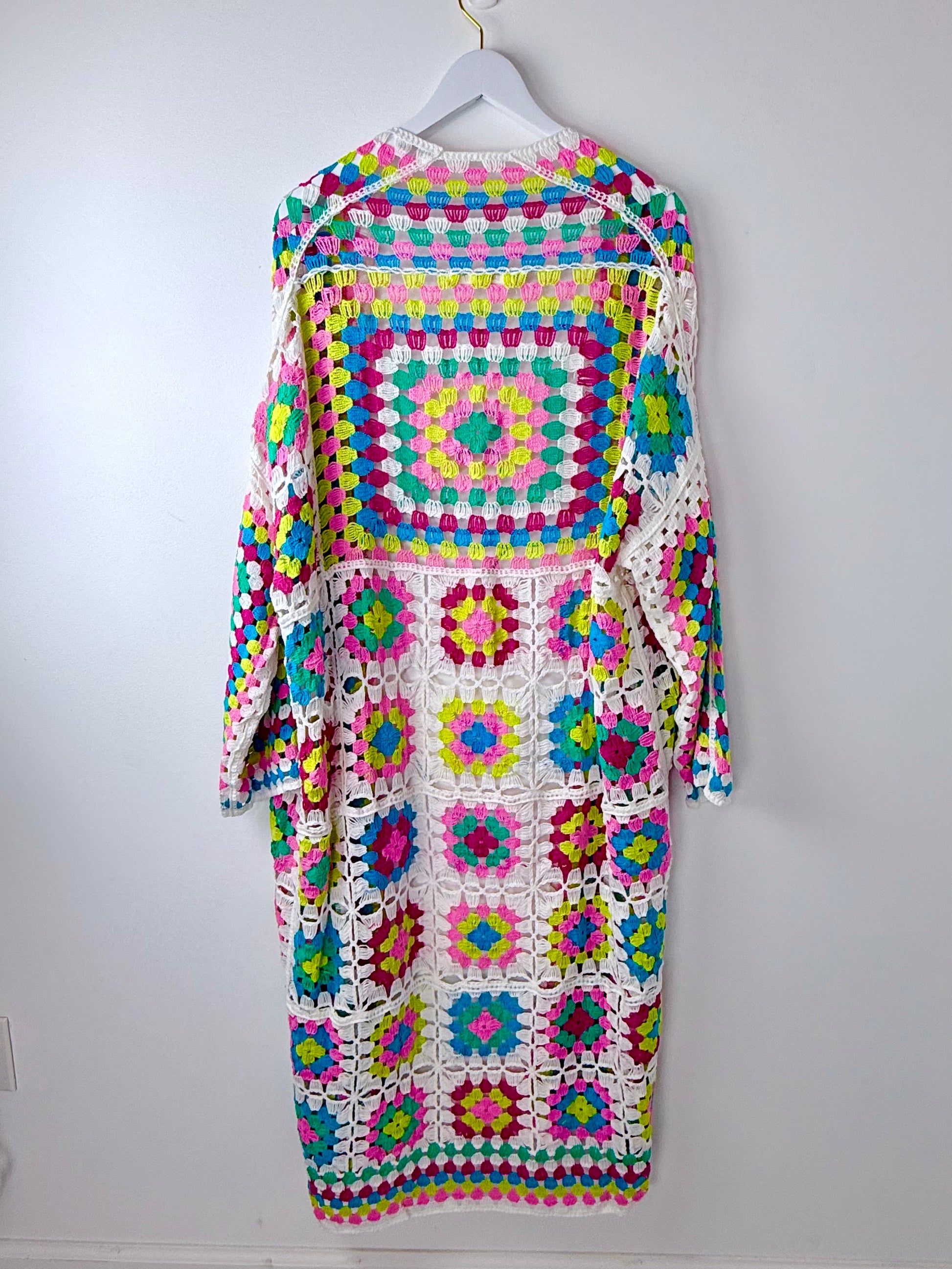 Colorful crocheted dress on a hanger against a white background
