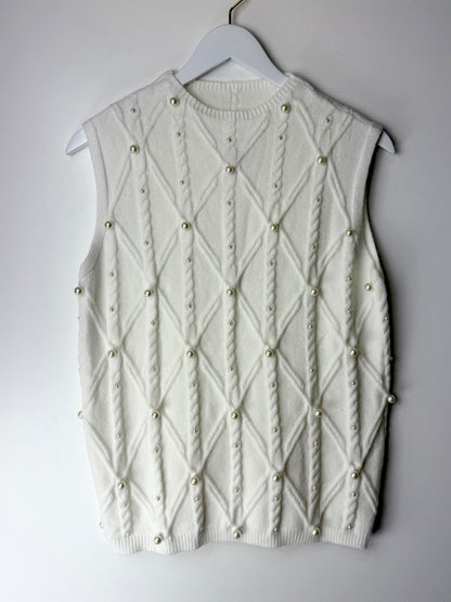 White sleeveless knitted vest with pearl embellishments on a hanger against a gray background