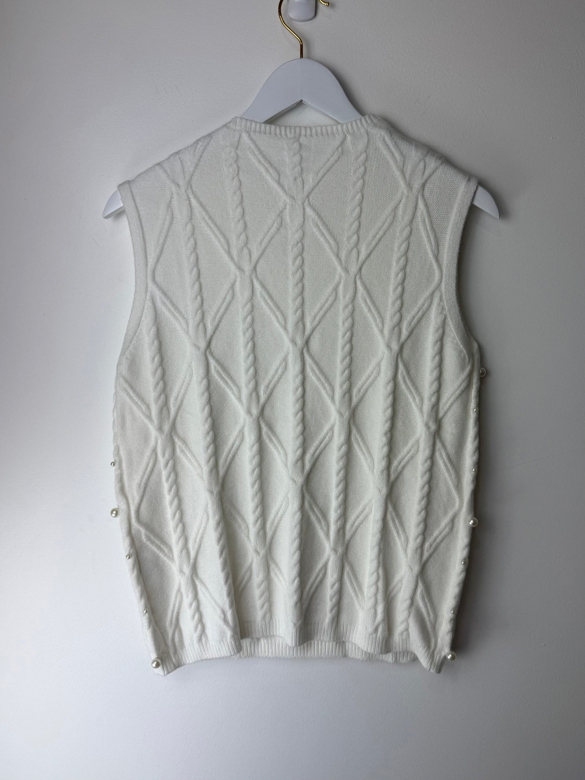 White knitted vest on a hanger against a plain background