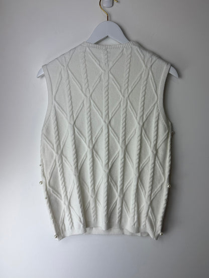 White knitted vest on a hanger against a plain background