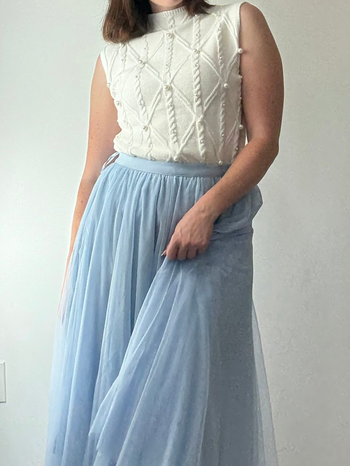 Person wearing a white textured top and light blue tulle skirt on a plain background