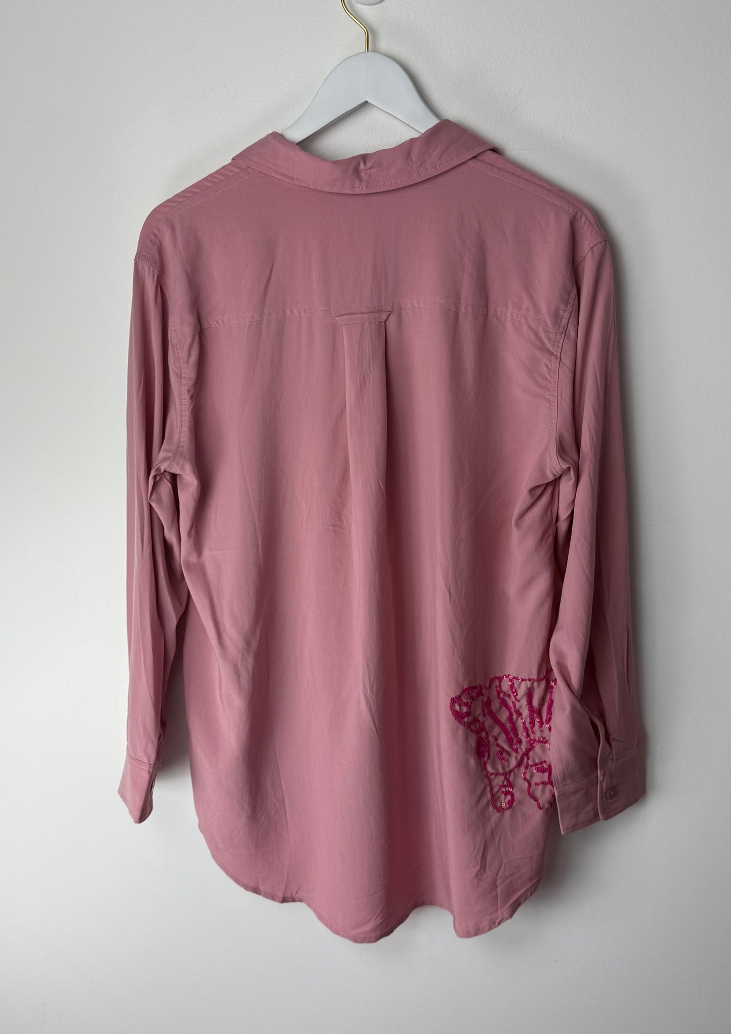 Pink shirt with pink sequin design on sleeve hanging on a white hanger against a white background