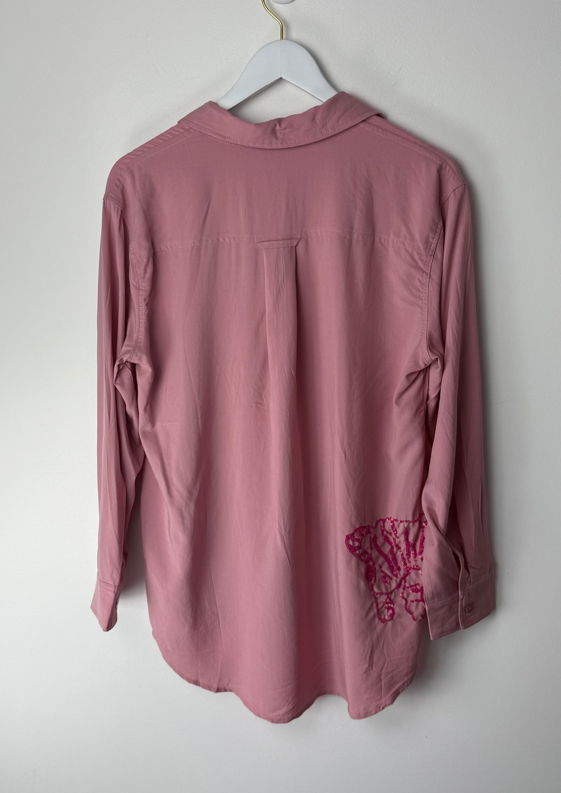 Pink shirt with pink sequin design on sleeve hanging on a white hanger against a white background