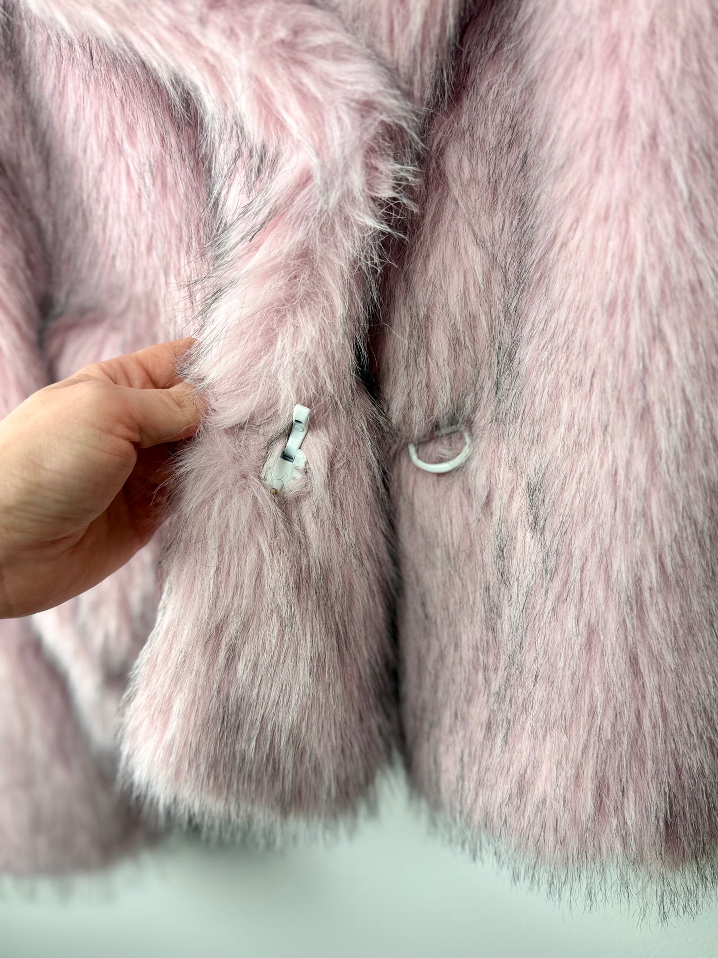 Close-up of a pink fur coat with a hand touching the fabric.