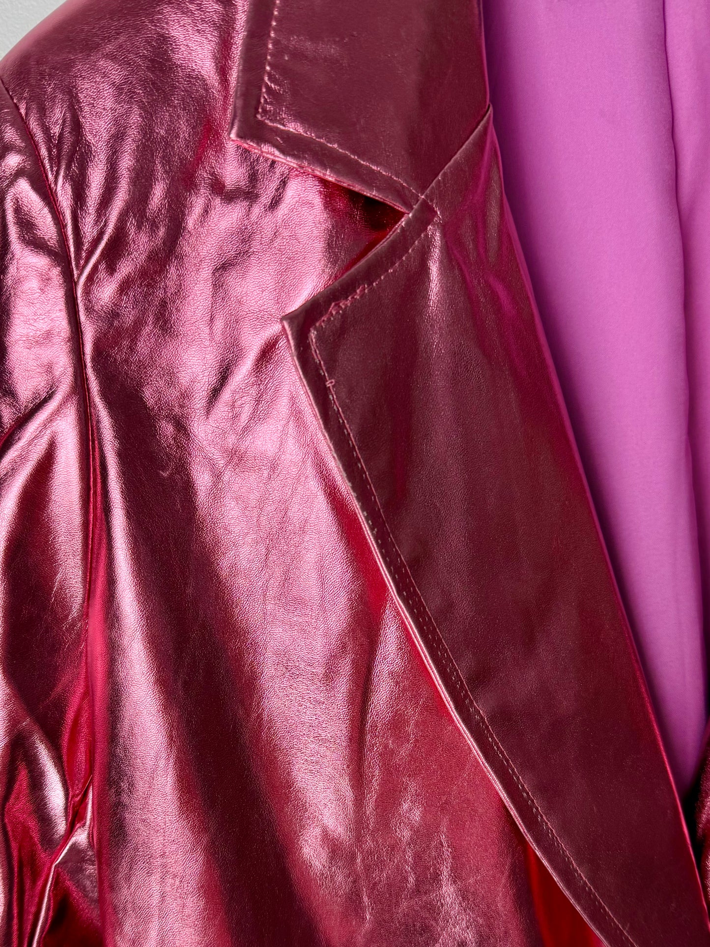 Close-up of a shiny metallic pink women’s leather jacket with a blurred pink background