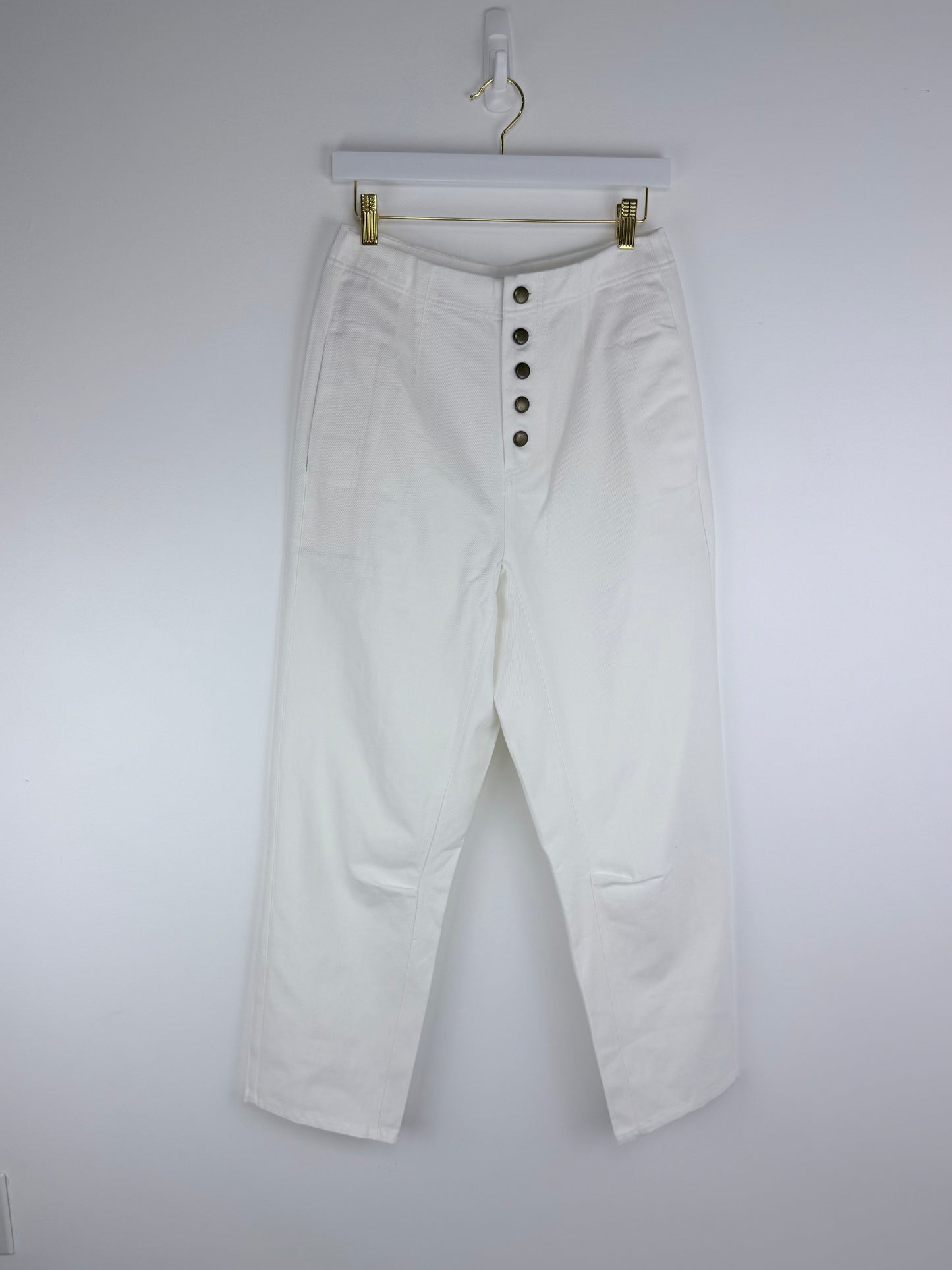 White pants with button details on a hanger against a white background