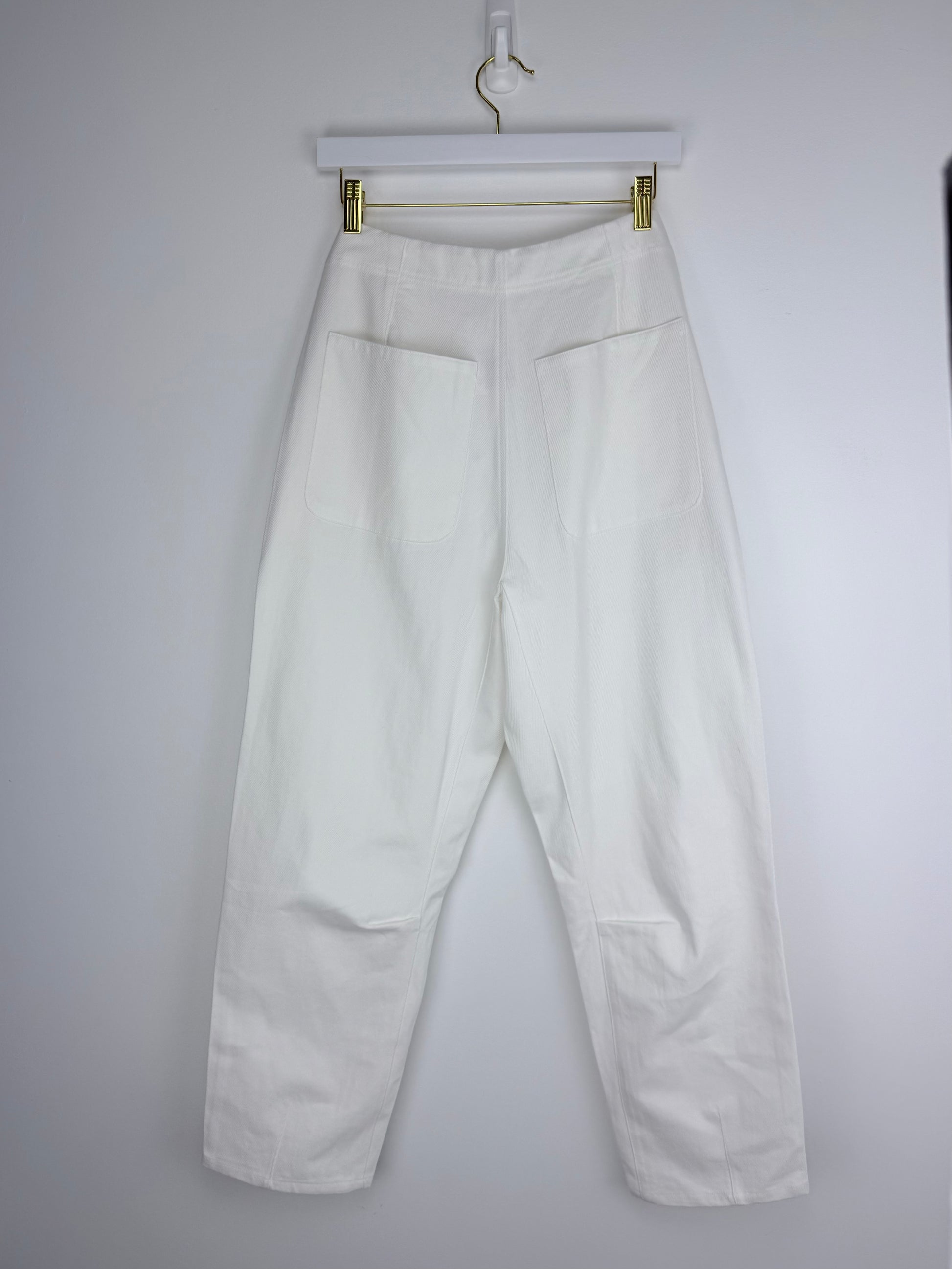 White pants hanging on a hanger against a plain background
