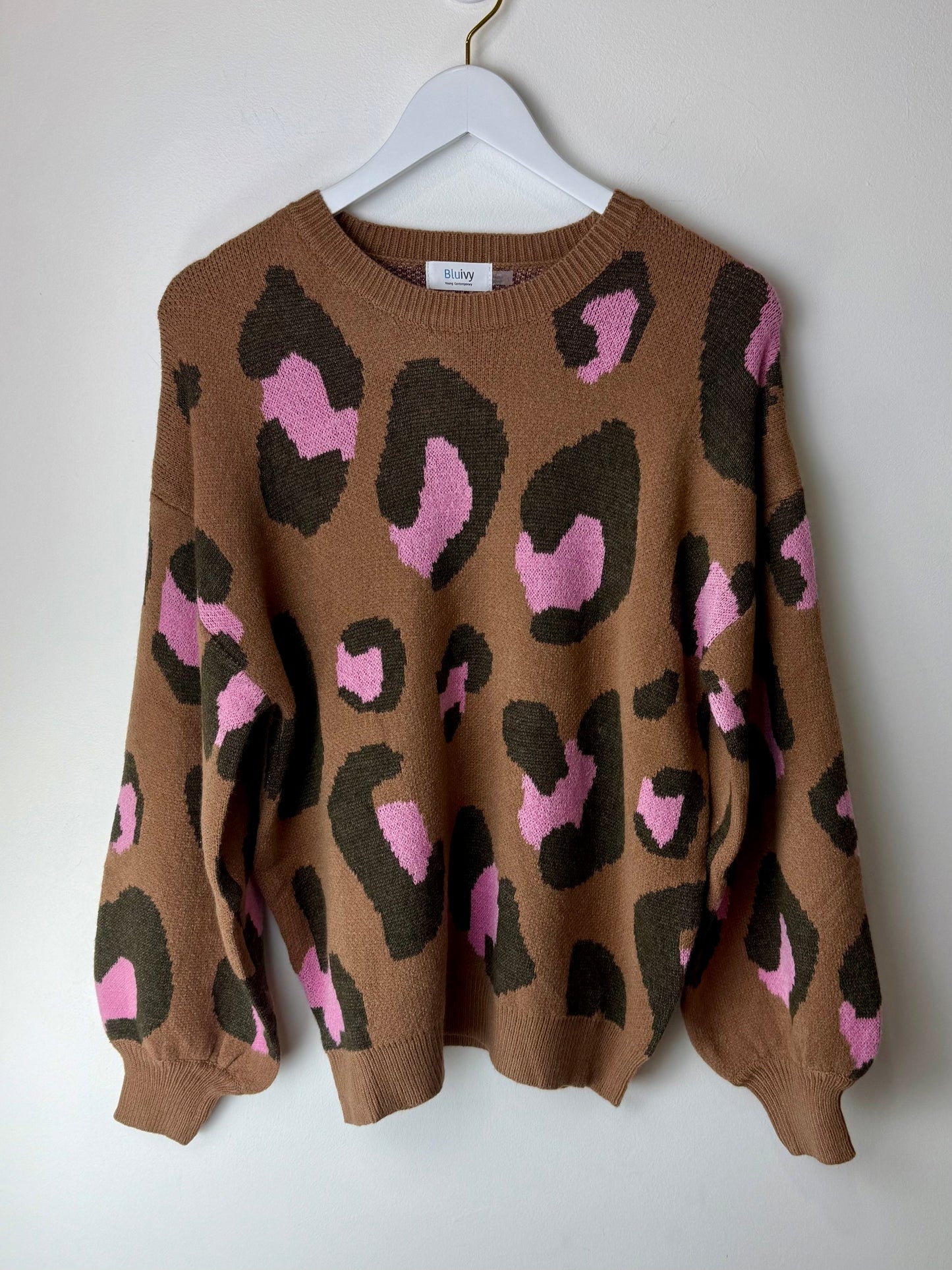 Brown sweater with pink and black leopard print on a white hanger against a white background