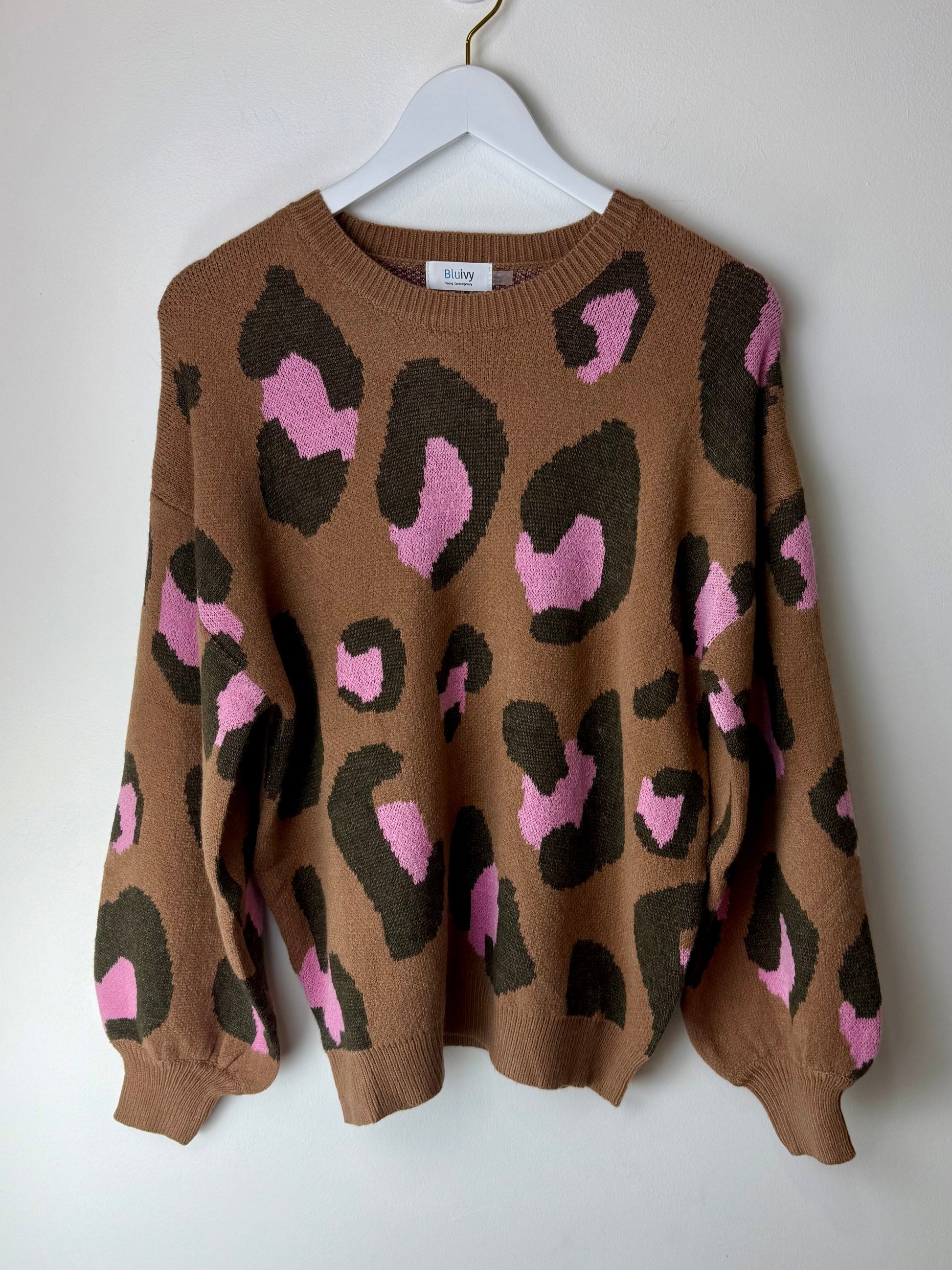Brown sweater with pink and black leopard print on a white hanger against a white background