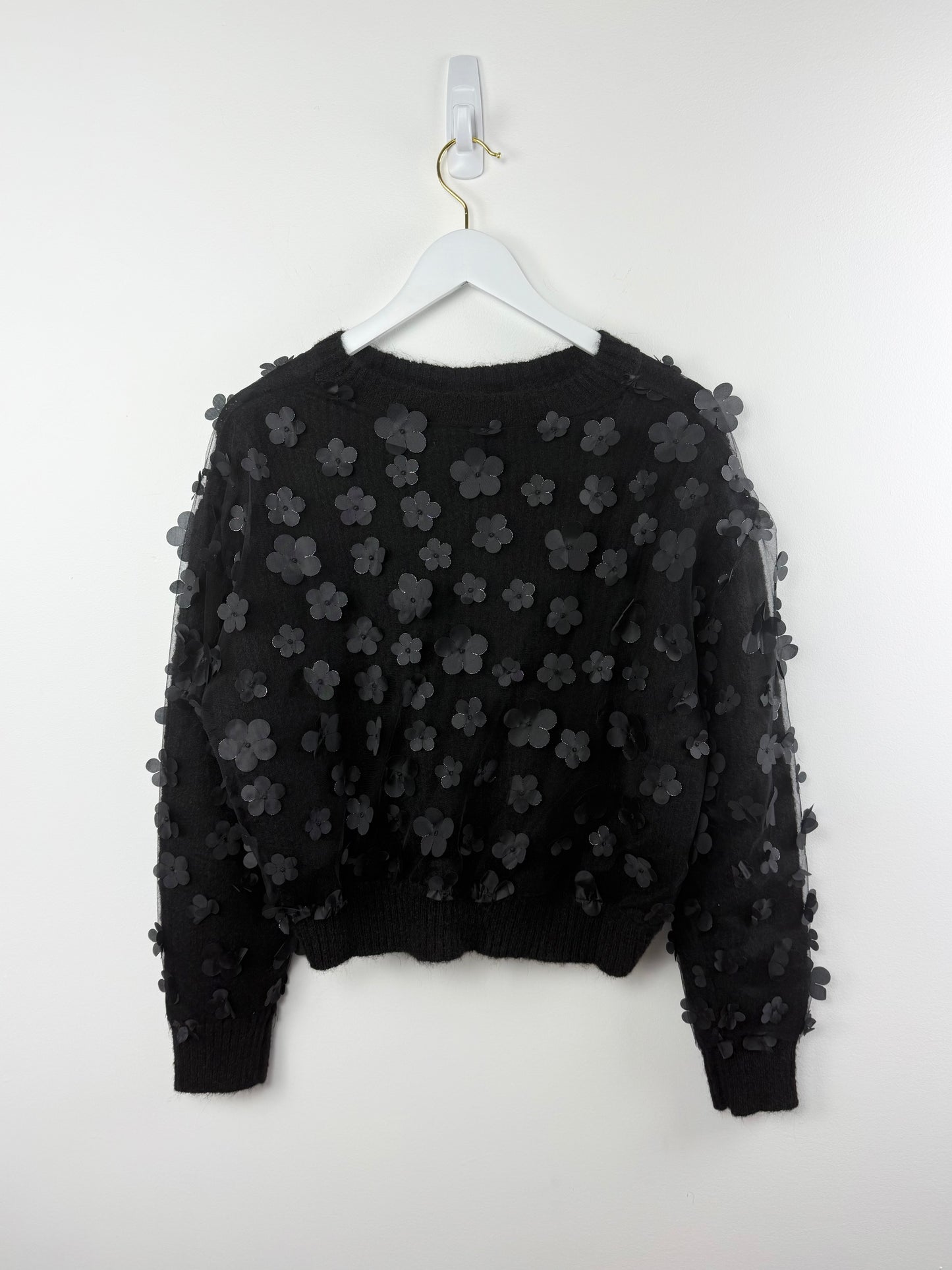 Black sweater with floral patterns on a white hanger against a white background