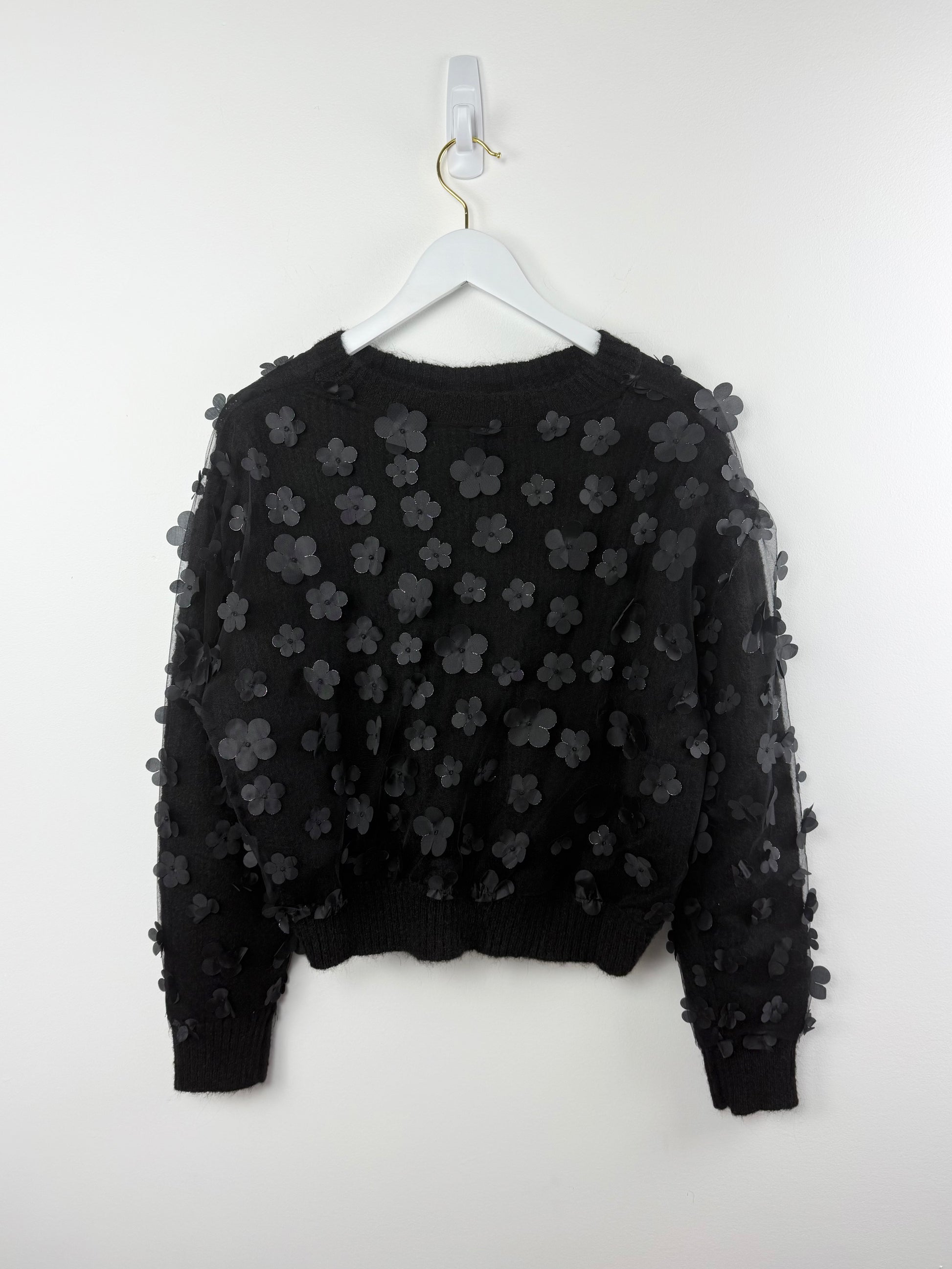 Black sweater with floral patterns on a white hanger against a white background