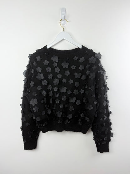 Black sweater with floral patterns on a white hanger against a white background