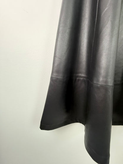 A close-up of a black leather or faux-leather garment, showing the draped fabric and a horizontal seam detail against a plain off-white background.