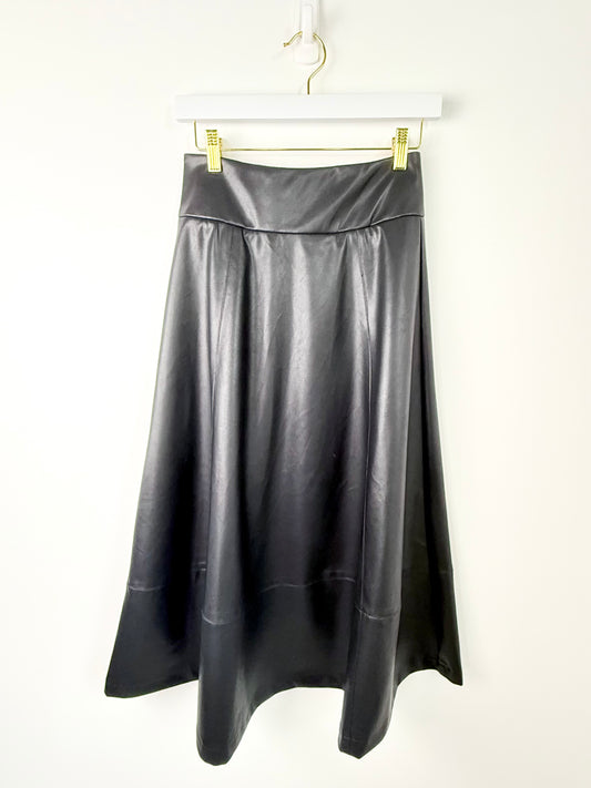 A black faux-leather A-line midi skirt hanging from a white hanger with gold clips against a plain white wall.